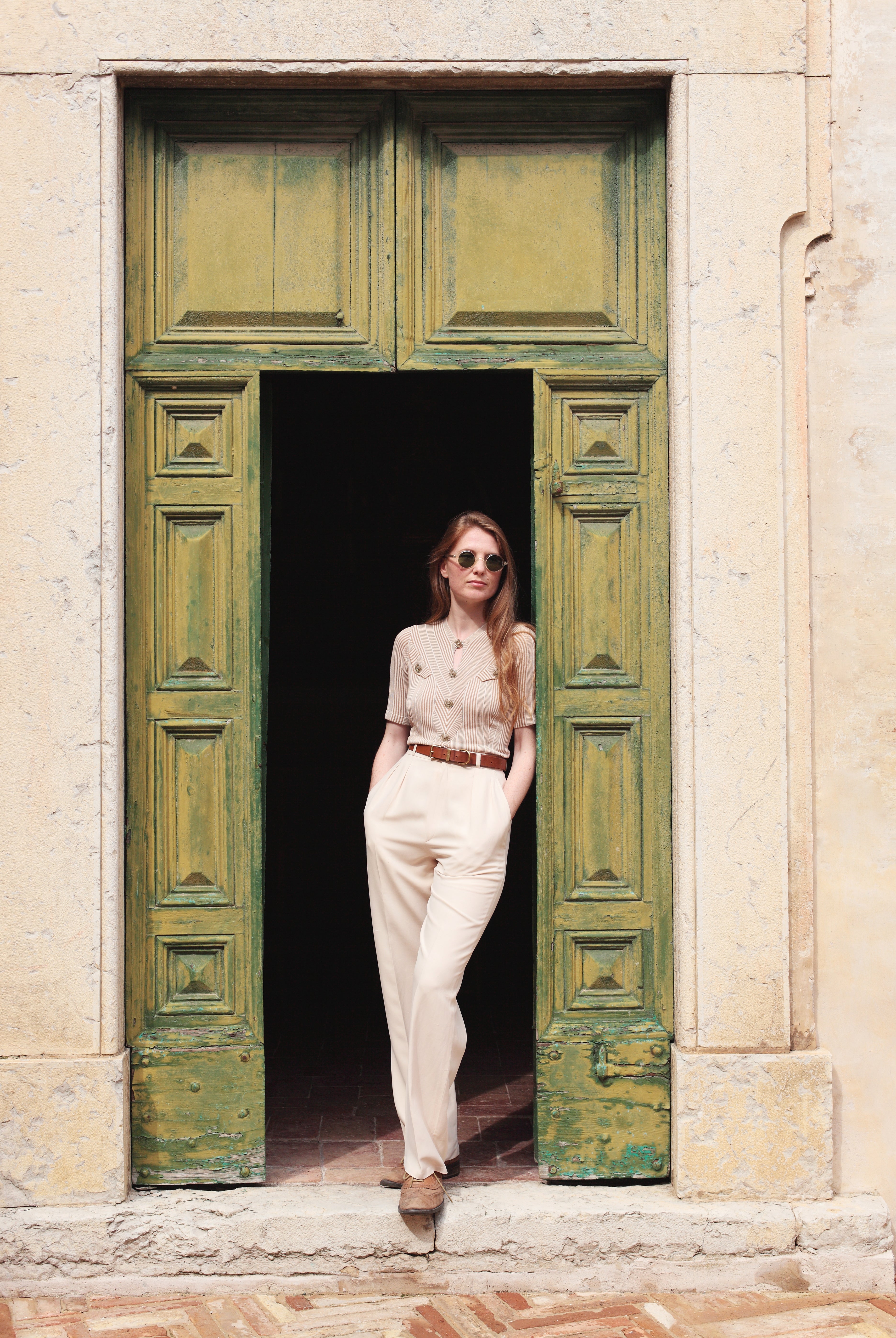Combelle Alix Top lifestyle shot, model in fawn colourway casually propped against green doorway, front three-quarter full-length view