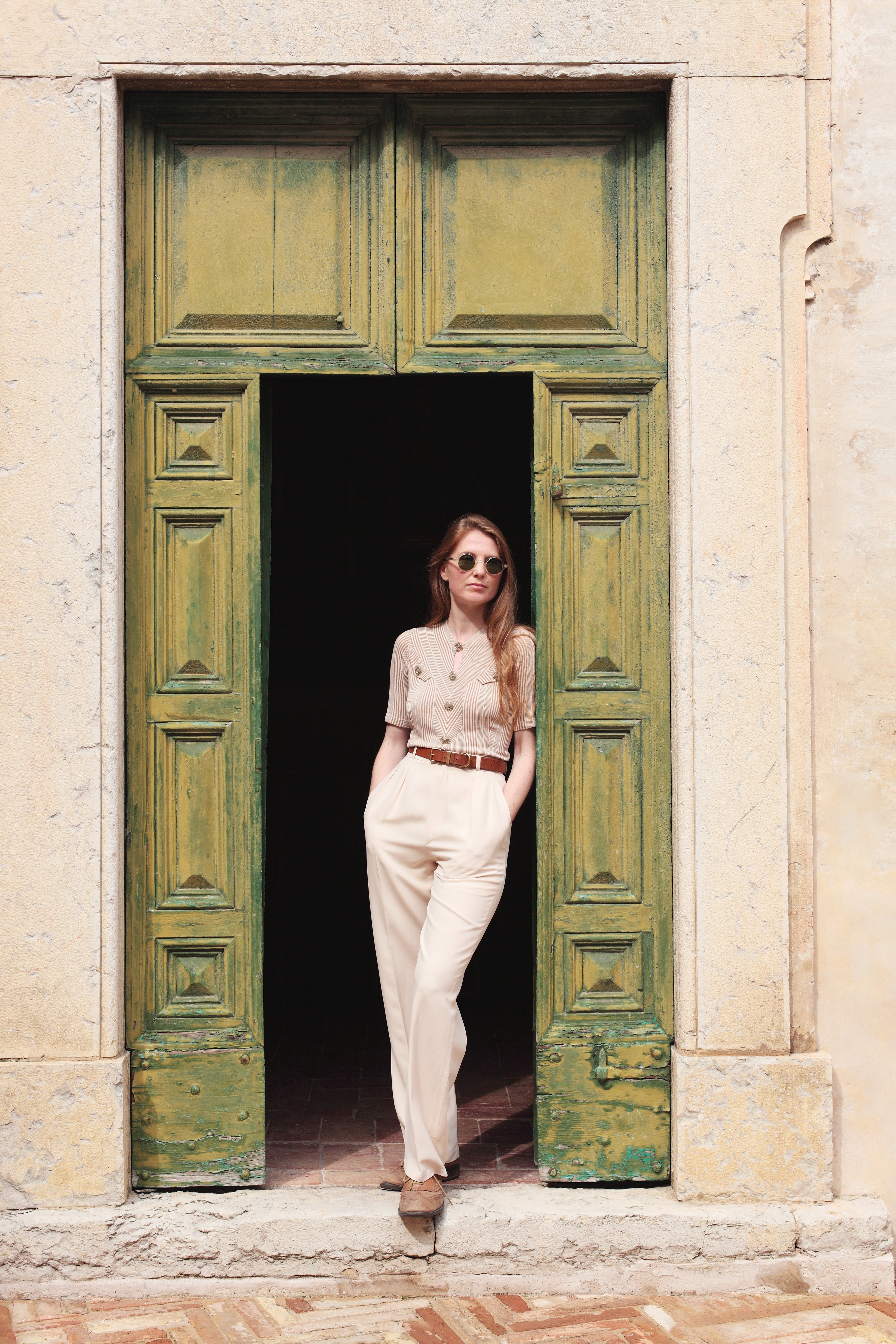 Combelle Alix Top lifestyle shot, model in fawn colourway casually propped against green doorway, front three-quarter full-length view
