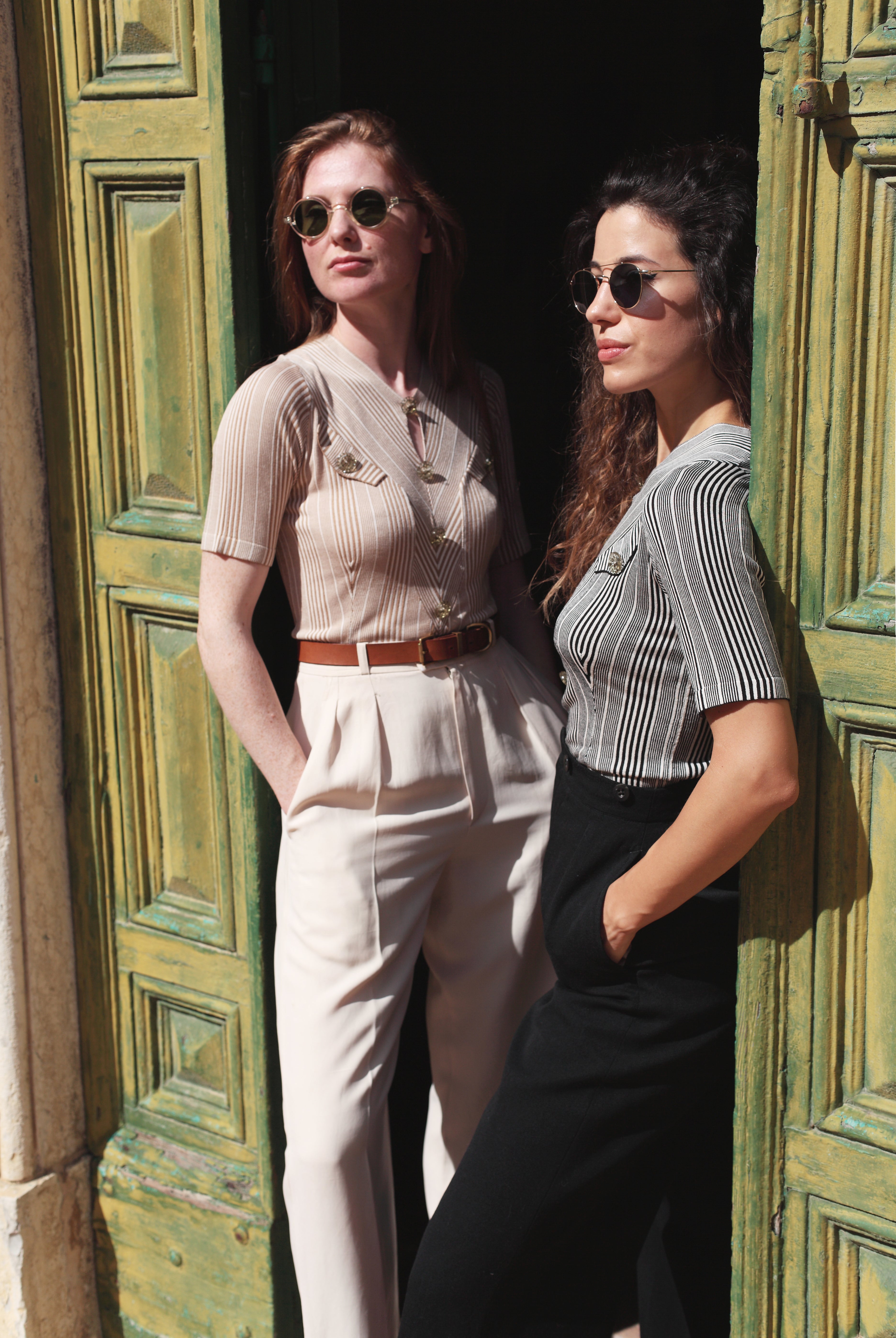 Combelle Alix Top lifestyle shot, two models lounging in green doorway wearing fawn and black colourways