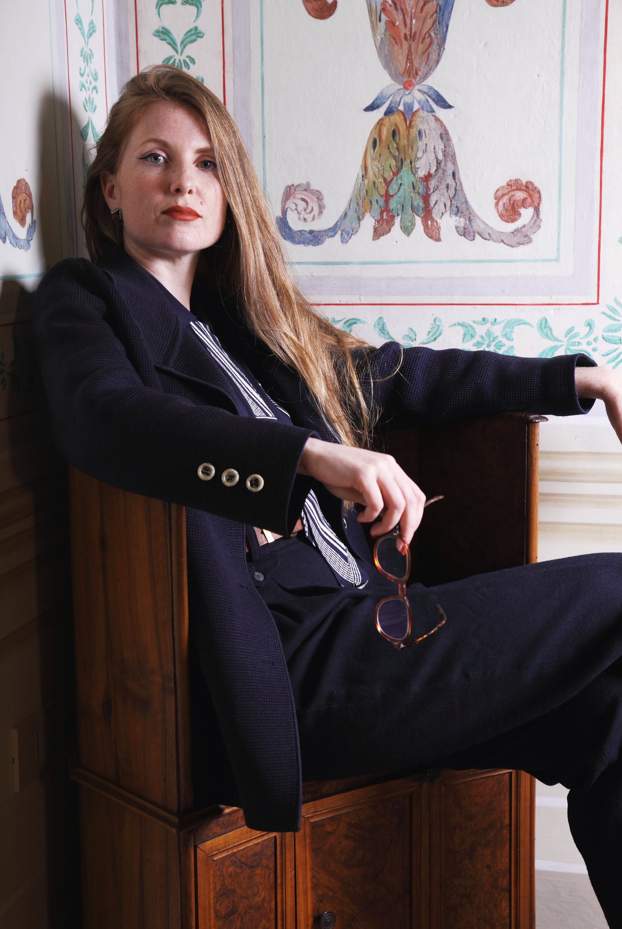 Combelle Eton Blouse navy lifestyle shot, model seated in decorative interior, three-quarter view