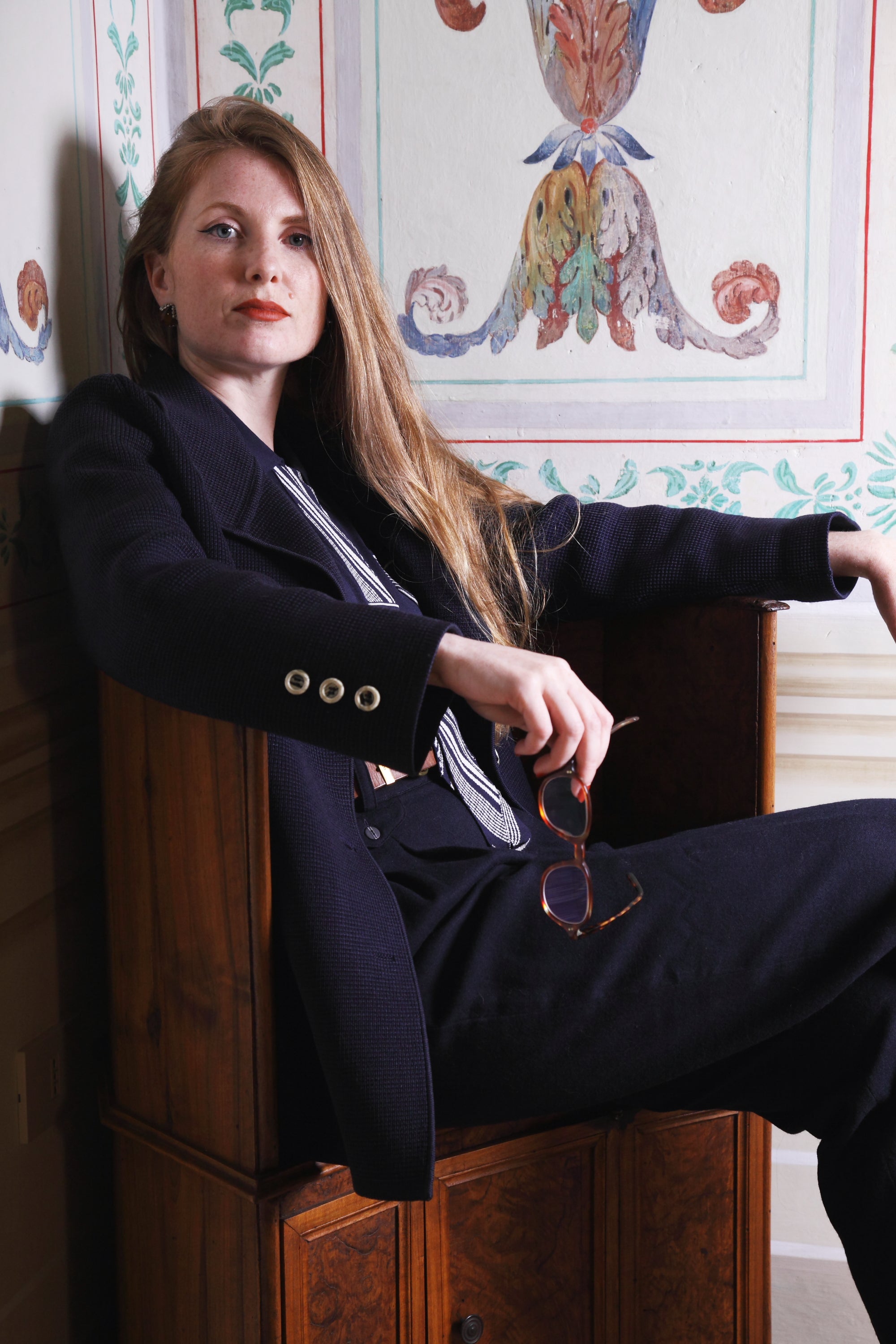 Combelle Eton Blouse navy lifestyle shot, model seated in decorative interior, three-quarter view