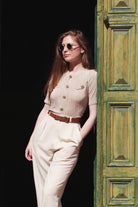 Combelle Alix Top lifestyle shot, model in fawn colourway casually propped against green doorway, front three-quarter upper body view
