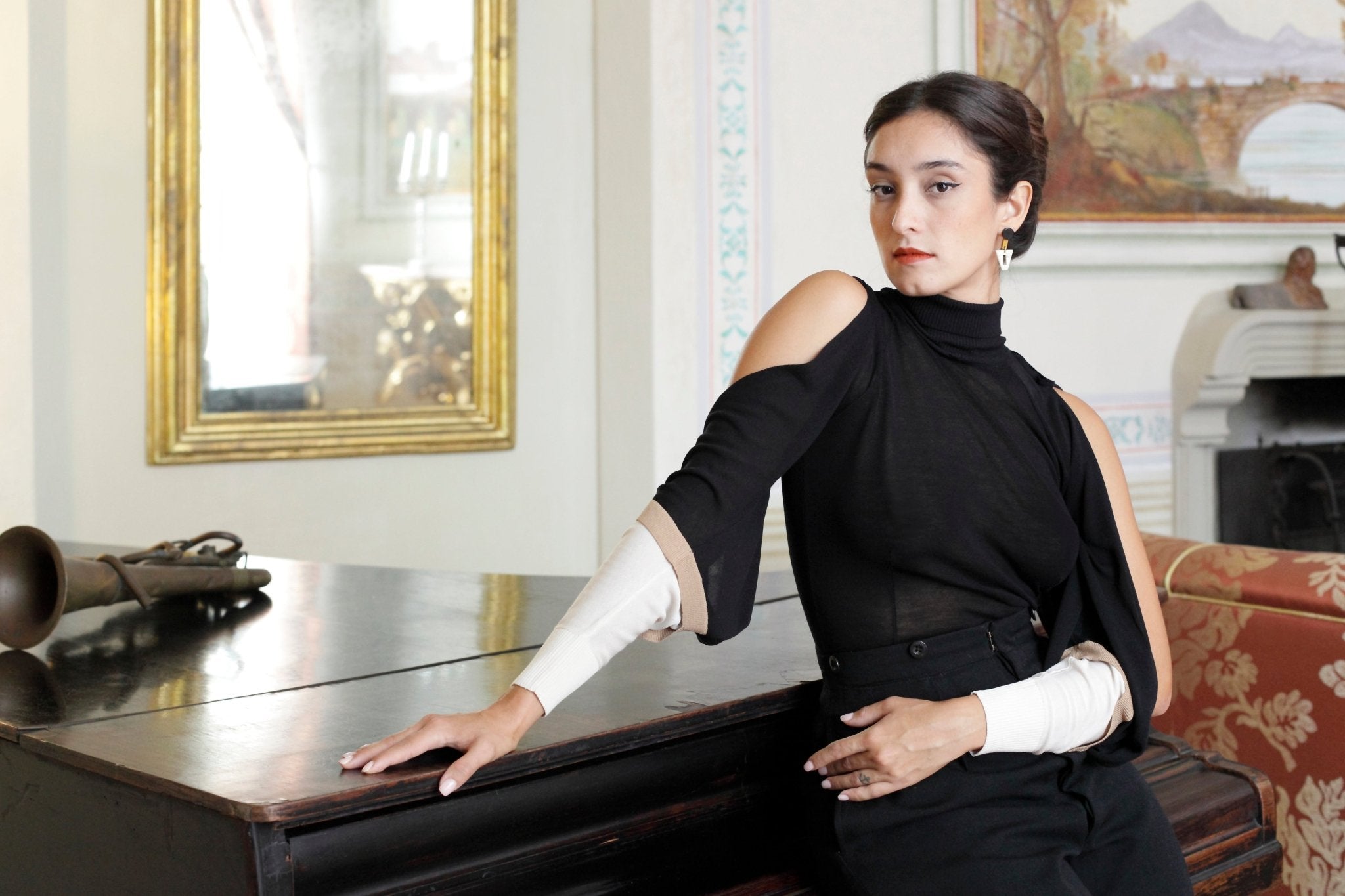 Combelle Elsa Top in black, side view seated in an ornate interior setting showing the sleeve drape and silhouette