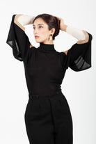 Combelle Elsa Top in black, front view with arms raised showing the dramatic open drape sleeve and high ribbed collar